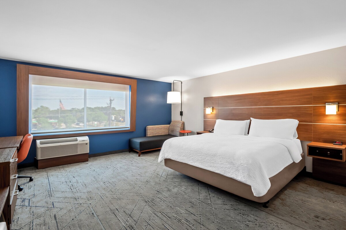 A modern hotel room with a large bed, a desk, and a view of a cityscape.
