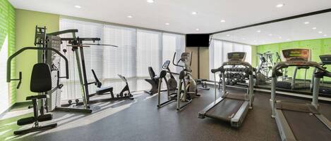 A gym with treadmills, weight machines, and a mirrored wall.