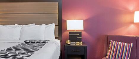 Una habitación de hotel con una cama, una mesita de noche con una lámpara y una silla con un cojín a rayas.