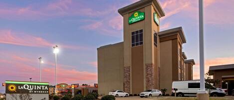 Un hotel La Quinta Inn & Suites con un letrero llamativo, un estacionamiento con varios coches y un cielo despejado.
