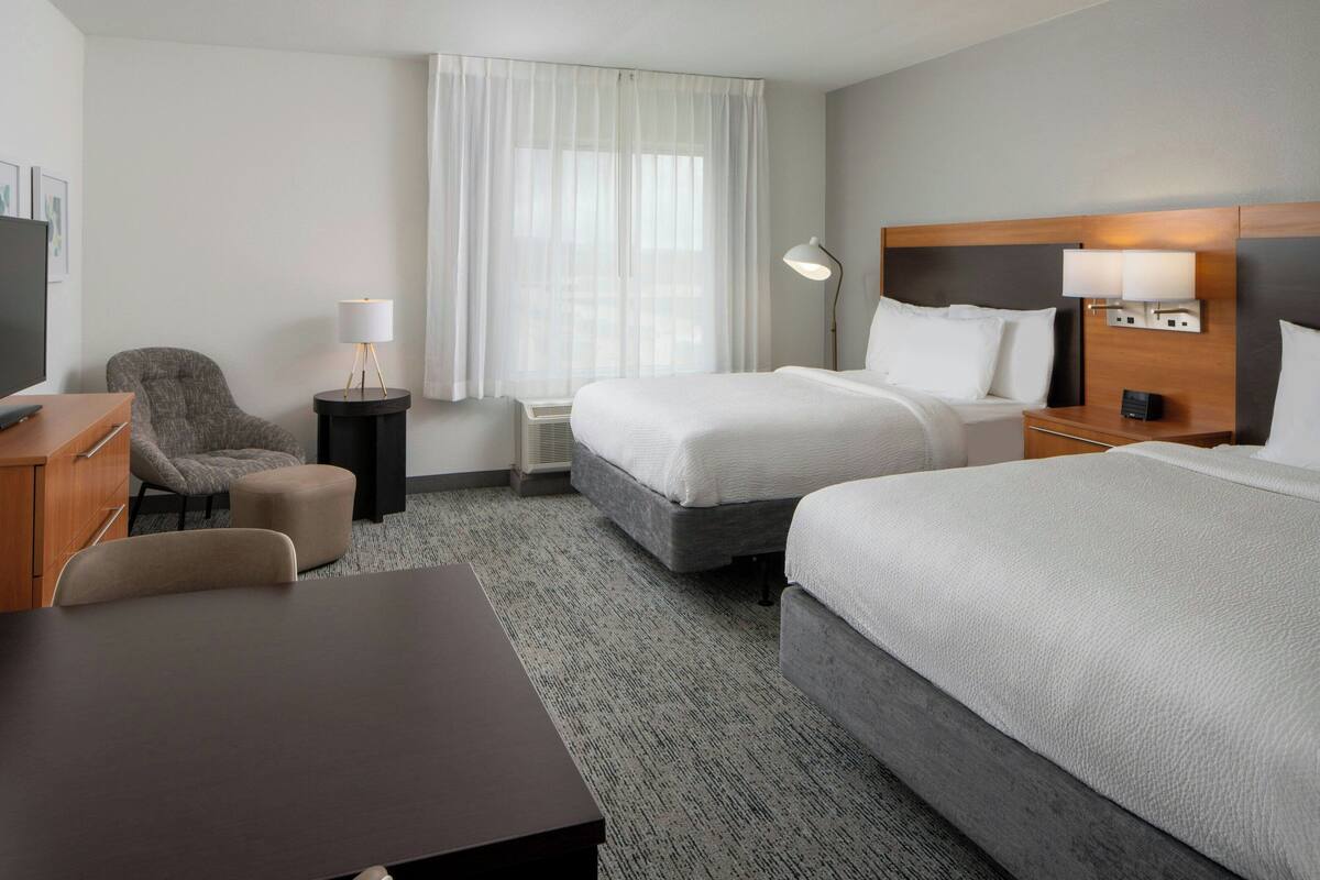 Hotelkamer met twee bedden, een bureau, een stoel, een televisie en een raam met gordijnen.