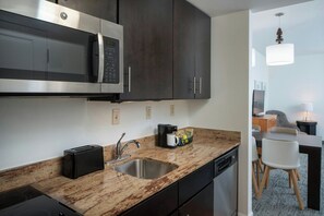A modern kitchen with dark cabinets, a stainless steel microwave, a sink, and a coffee maker.