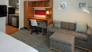 Une chambre d’hôtel équipée d’une kitchenette, d’un bureau avec une chaise, d’un canapé et de deux œuvres d’art encadrées au mur.