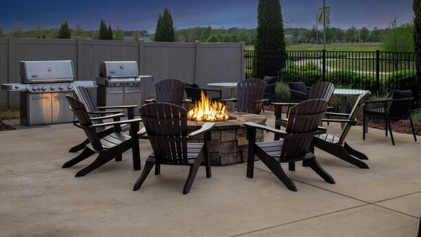 Une terrasse extérieure avec un foyer en pierre, des fauteuils Adirondack et un barbecue.