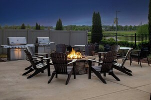 Un patio al aire libre con un hogar a leña de piedra, sillas Adirondack y una parrilla.