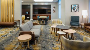 Un hall d’hôtel moderne avec un canapé, des fauteuils, une petite table, un téléviseur et une bibliothèque.