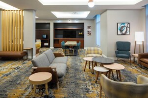 Un moderno hall de hotel con un sofá, sillas, una mesita, un televisor y una estantería.