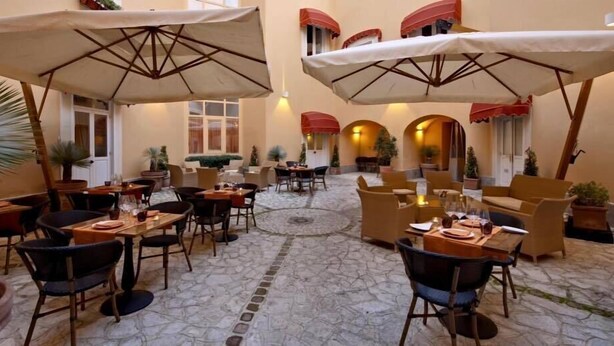 An outdoor café with tables and chairs, umbrellas, and potted plants. - San Leucio Resort (Caserta)