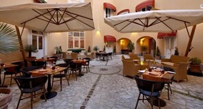 An outdoor café with tables and chairs, umbrellas, and potted plants. - San Leucio Resort (Caserta)