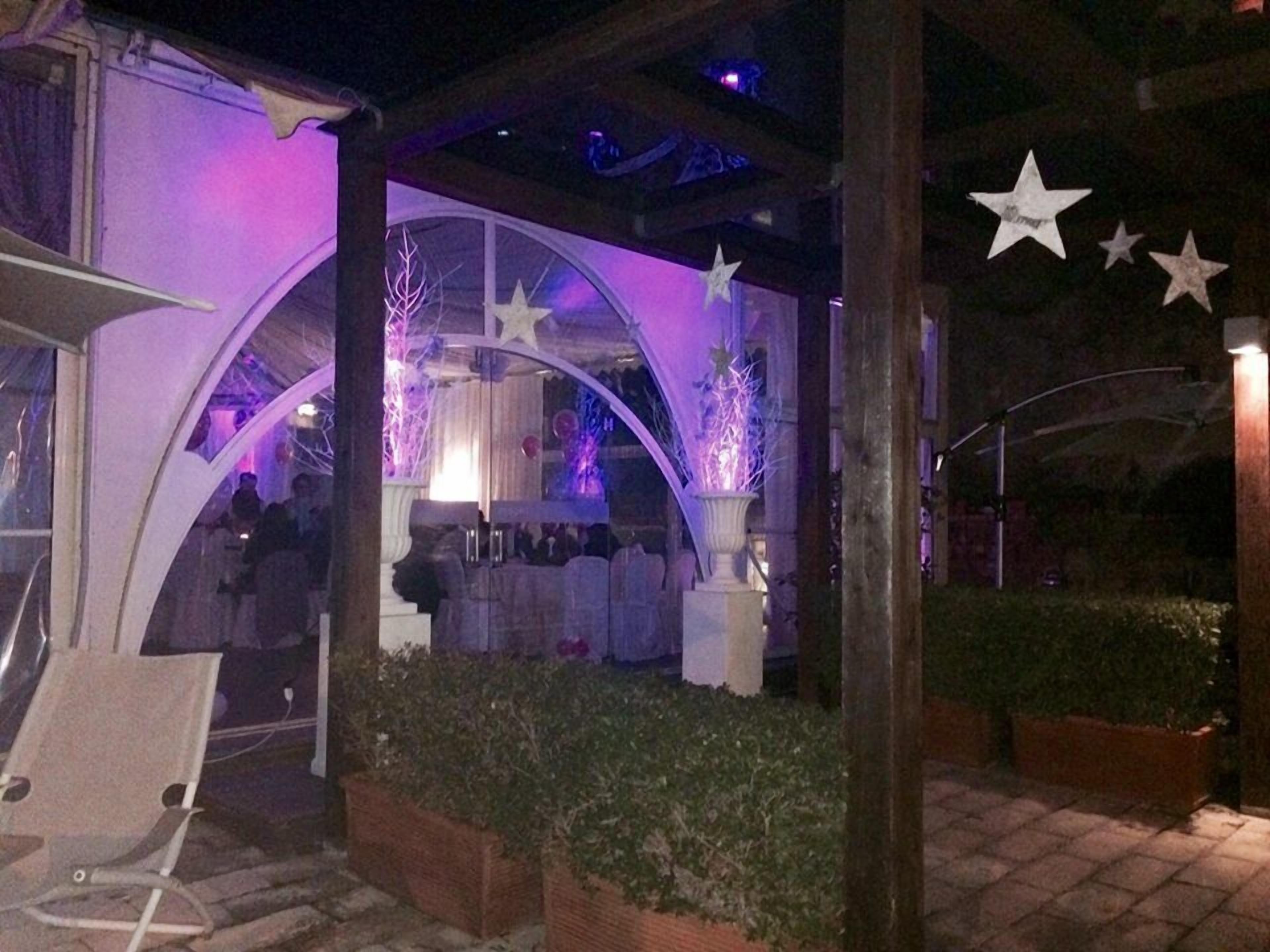 Ein möblierter Patio-Bereich im Freien mit überdachtem Sitzbereich, dekorativer Beleuchtung in Form von Sternen und einem gepflegten Garten.