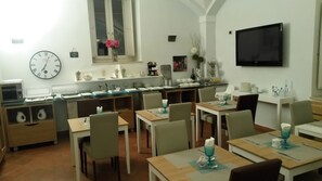 A dining area with multiple tables and chairs, a clock on the wall, and a television mounted on the wall.