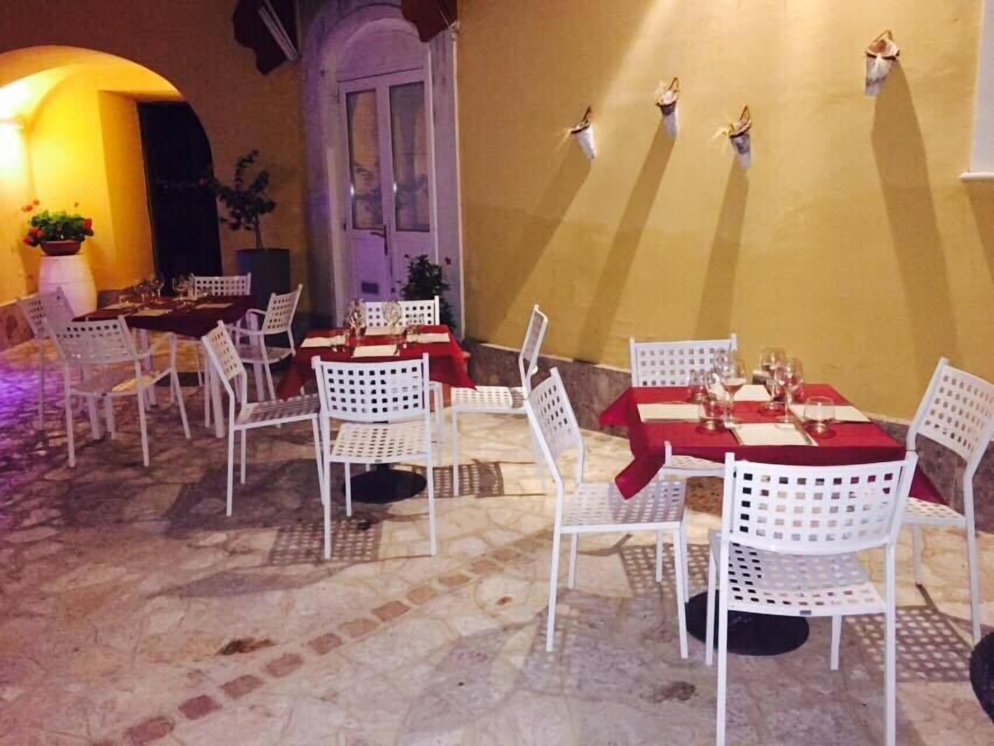 Un área de comedor al aire libre con sillas y mesas de metal blanco, cada conjunto con manteles rojos y copas de vino.