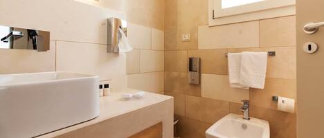 Een moderne badkamer met een groot wit wastafelmeubel, een spiegel, een handdoekrek en een klein wit zuiltje met wastafel.