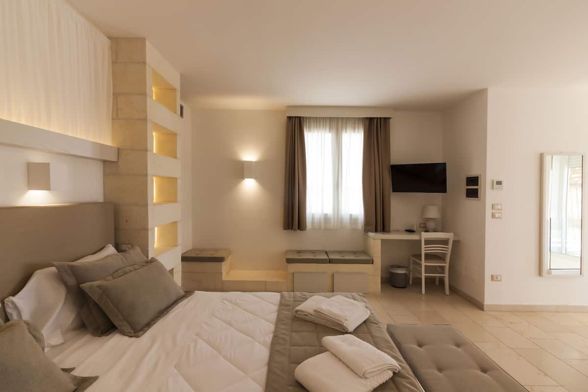 A modern hotel room with a large bed, a desk, a chair, and a TV.