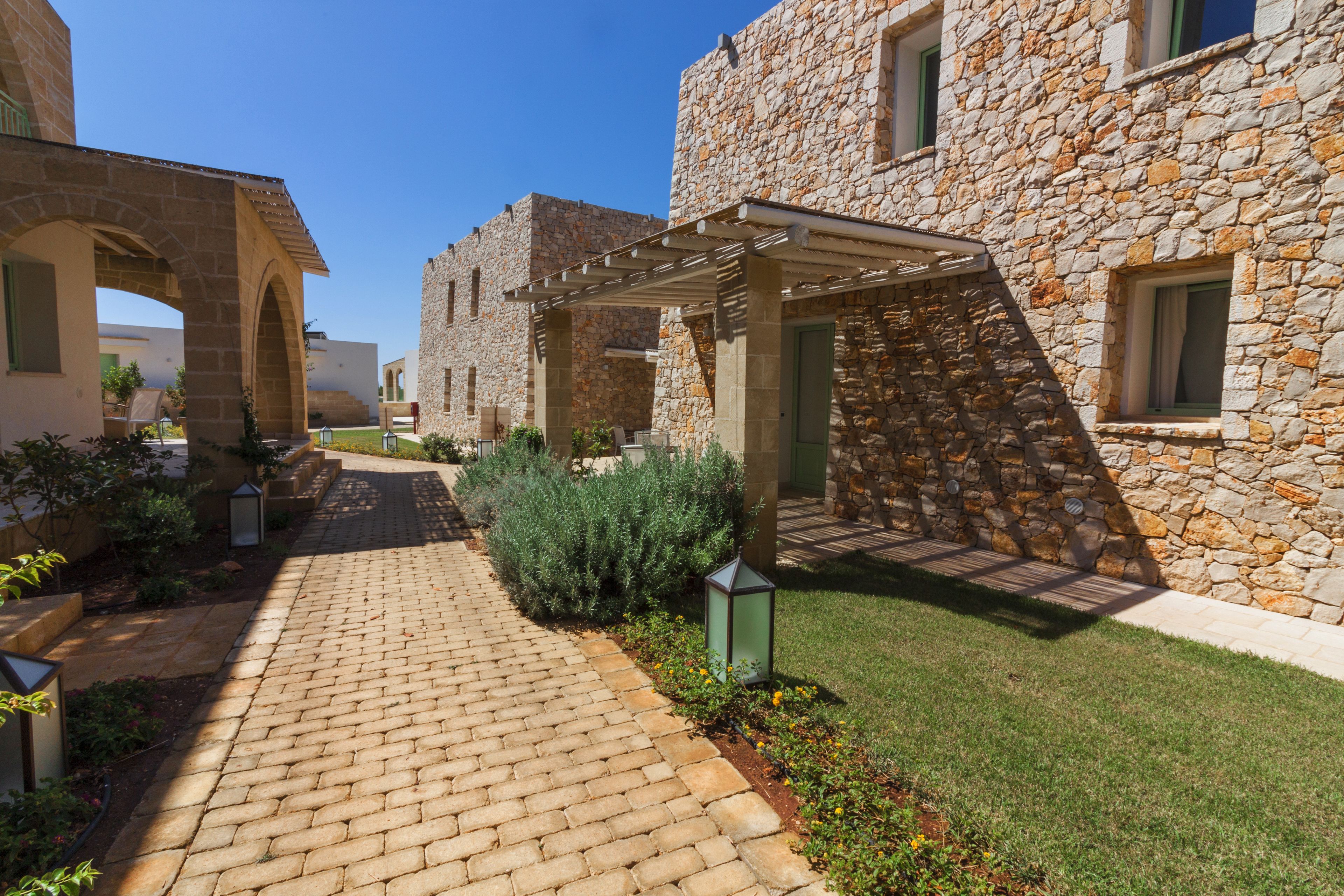 A courtyard with stone buildings, a paved walkway, and a pergola.