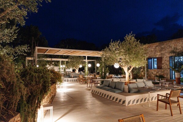 An outdoor dining area with tables and chairs, a covered seating area, and a stone building in the background. - Tenuta Montiró (Castrignano del Capo)