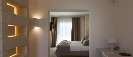 A hotel room with a bed, a desk, a lamp, and a wall-mounted light fixture.