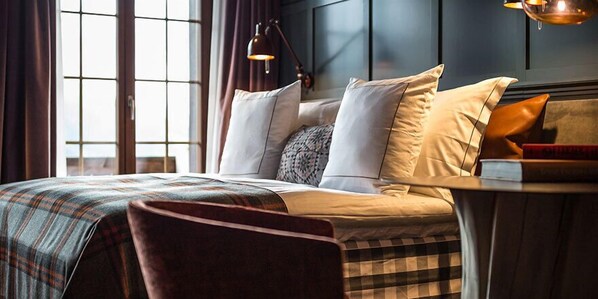 A modern hotel room with a large bed, a bedside table, and a window with curtains. - HUUS Gstaad (Saanen)
