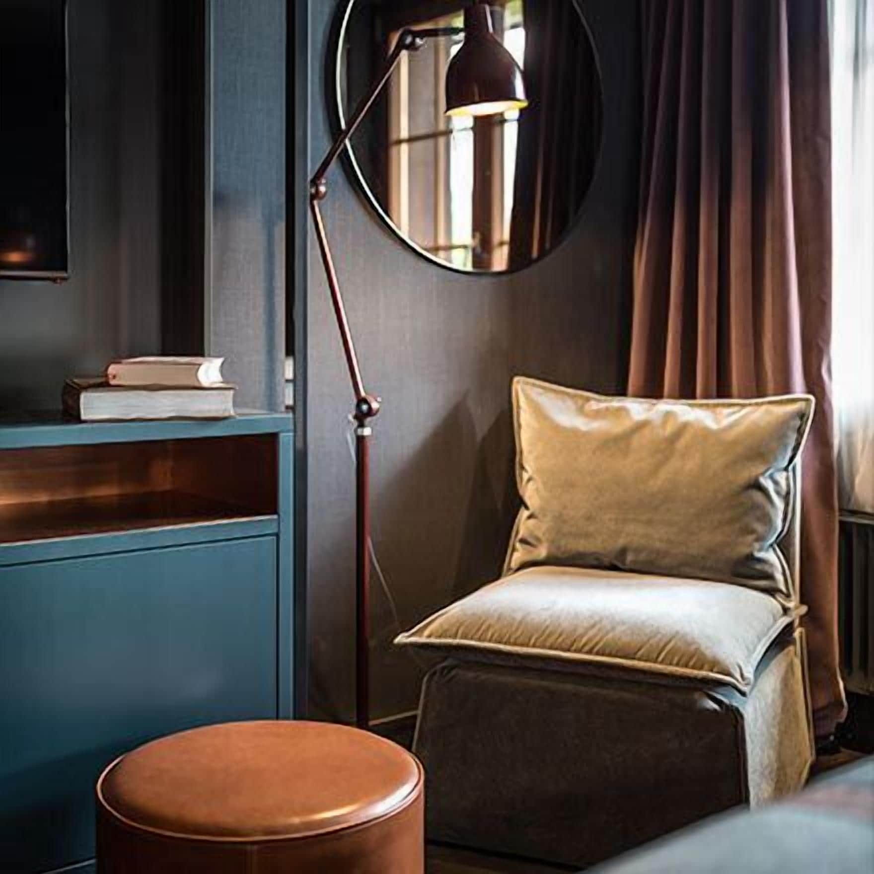 A room with a blue cabinet, a round floor lamp, a cushioned chair, and a round ottoman.