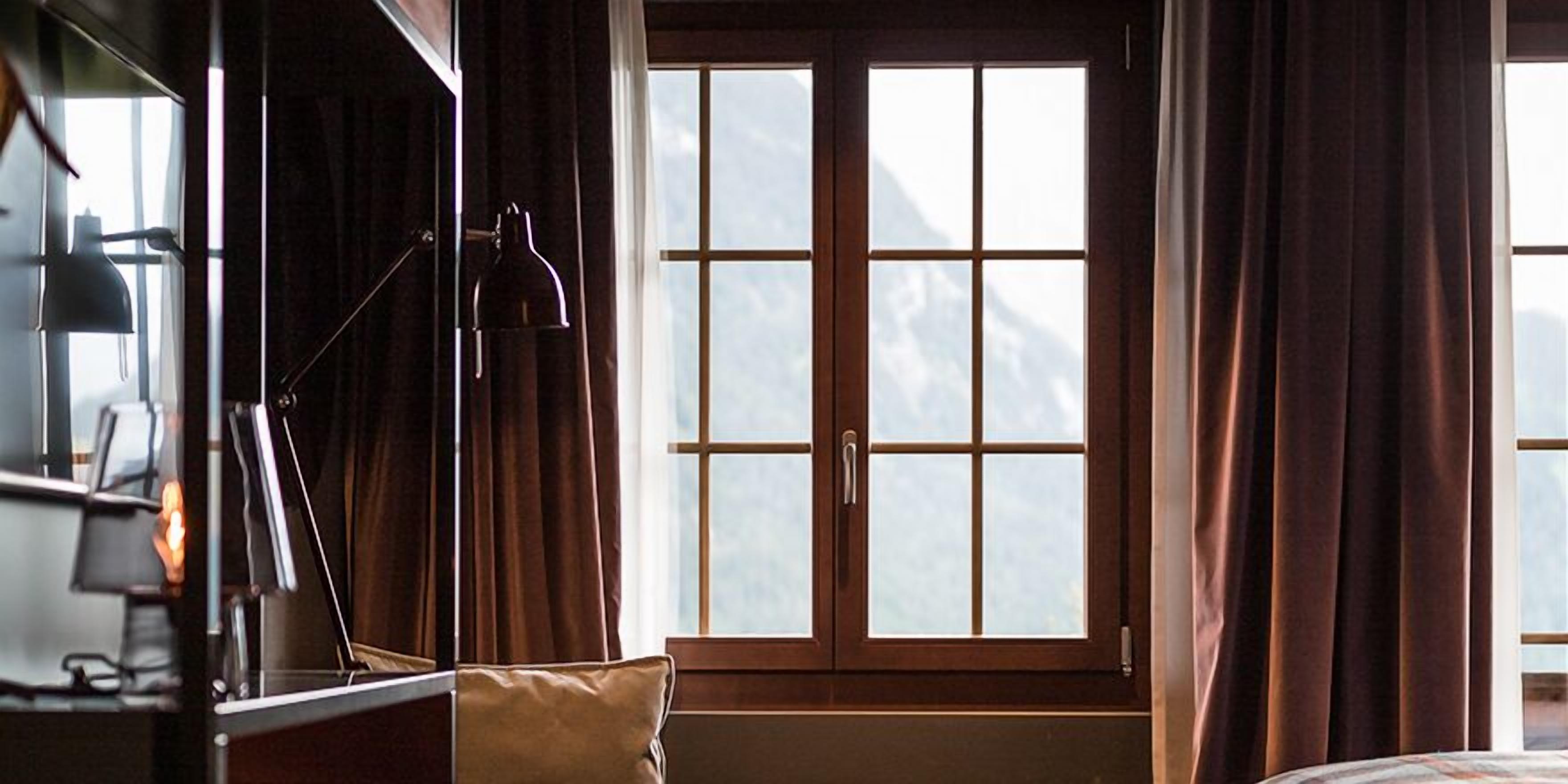 A hotel room with a large window, a desk with a lamp, and a bed.