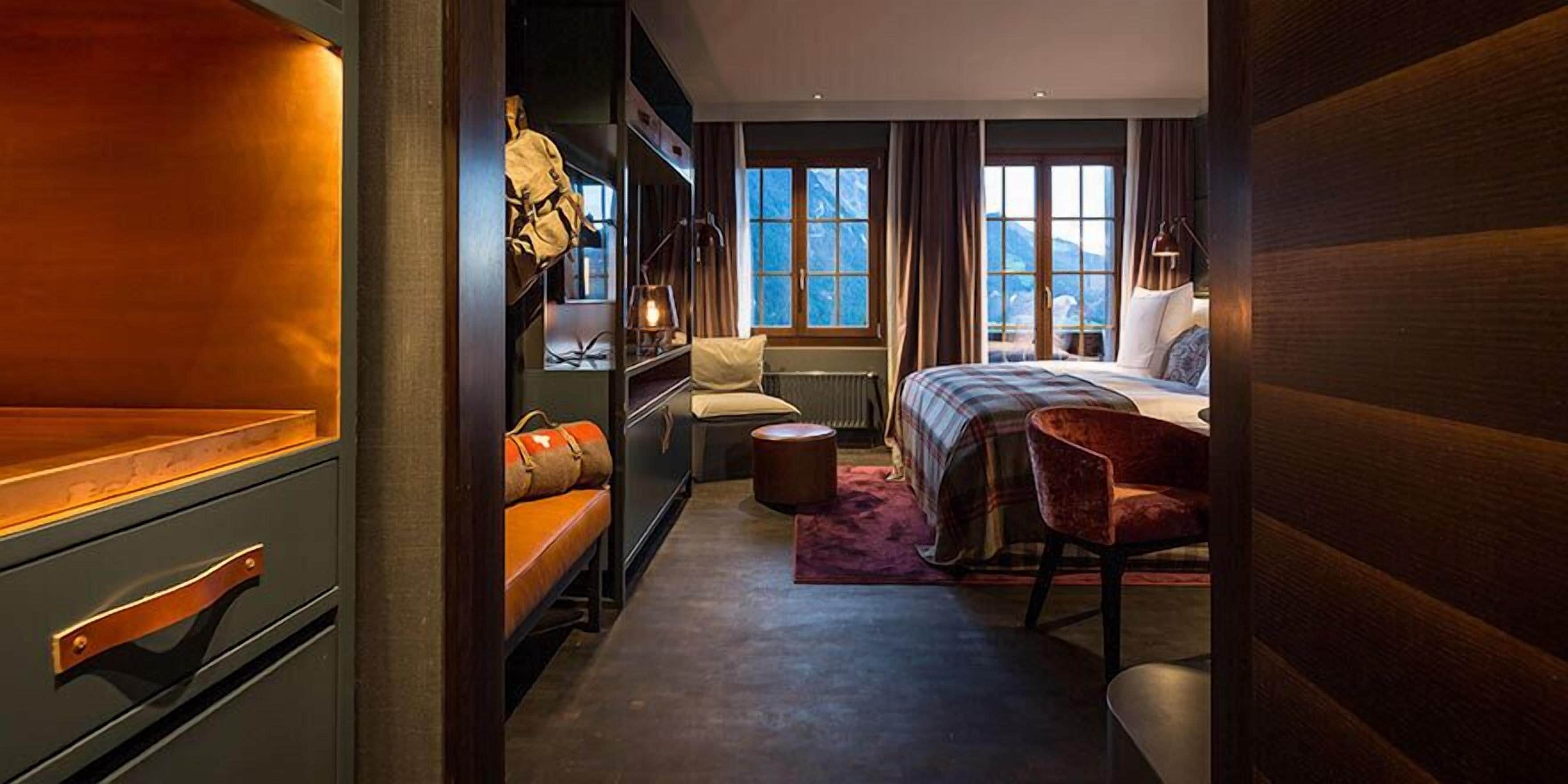 A cozy hotel room with a bed, a chair, a small table, and a bench.