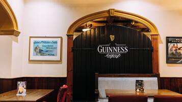 A bar area with a Guinness sign, a framed poster of James McAllister & Son's Old Irish Whiskey, and a welcome sign.
