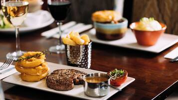A dining table with a steak, onion rings, and a small bowl of sauce.
