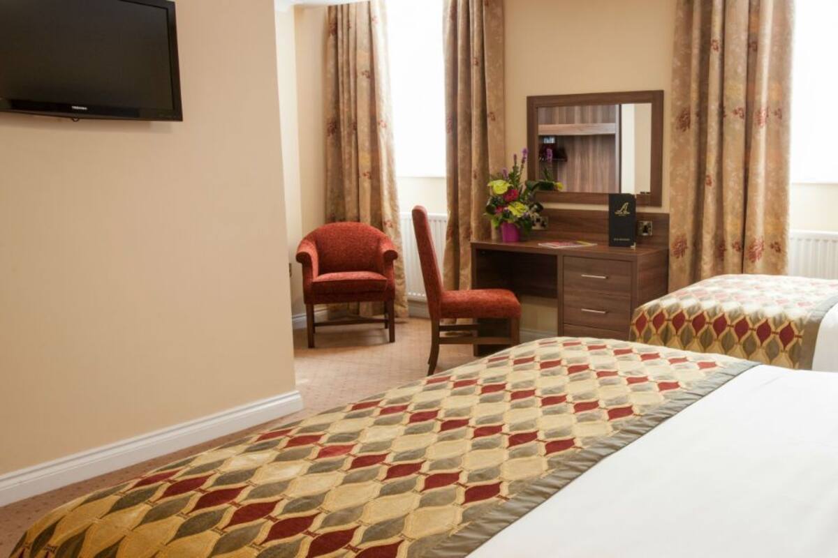 A hotel room with two beds, a desk with a chair, a television, and a window with curtains.