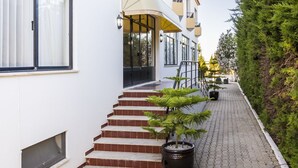 Un edificio con una escalera que conduce a un porche cubierto, una planta en maceta y un sendero junto a un seto.