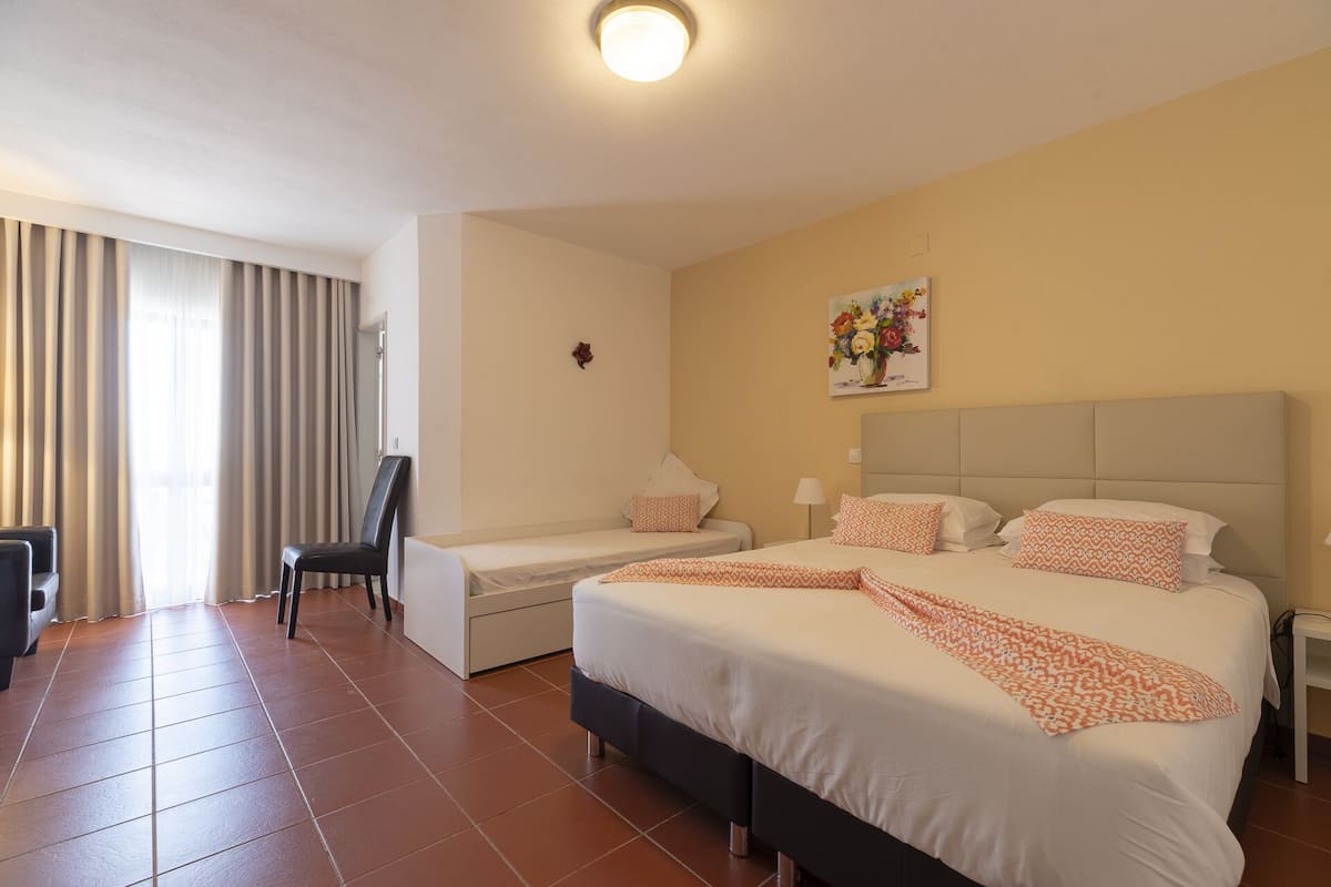 A hotel room with a large bed, two bedside tables, a chair, a desk, and a window with curtains.
