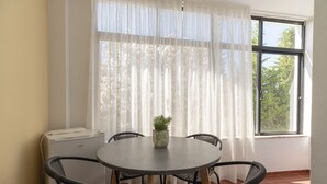 Una mesa redonda con cuatro sillas, una planta en maceta y una ventana con cortinas translúcidas.