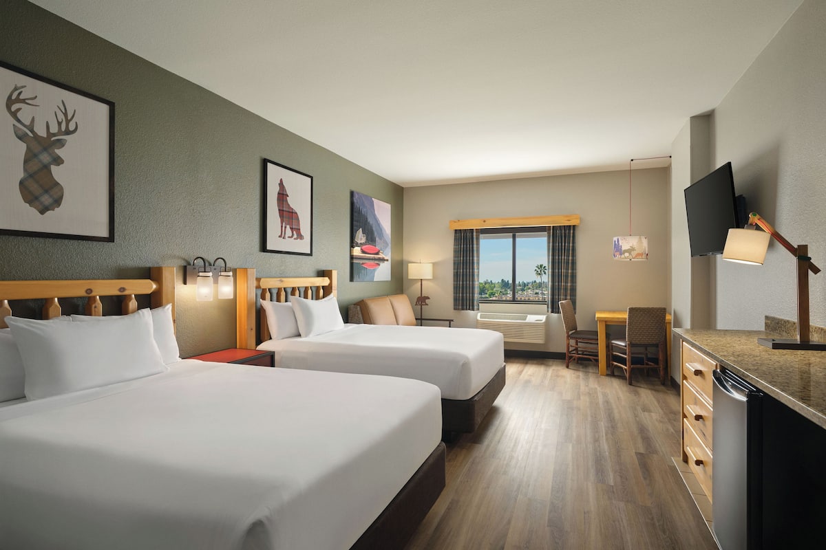 A hotel room with two beds, a desk, a chair, a television, and artwork on the walls.
