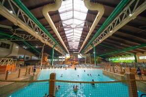 An indoor swimming pool with a high ceiling, visible structural beams, and a central water slide. - Great Wolf Lodge Anaheim, CA (Garden Grove)