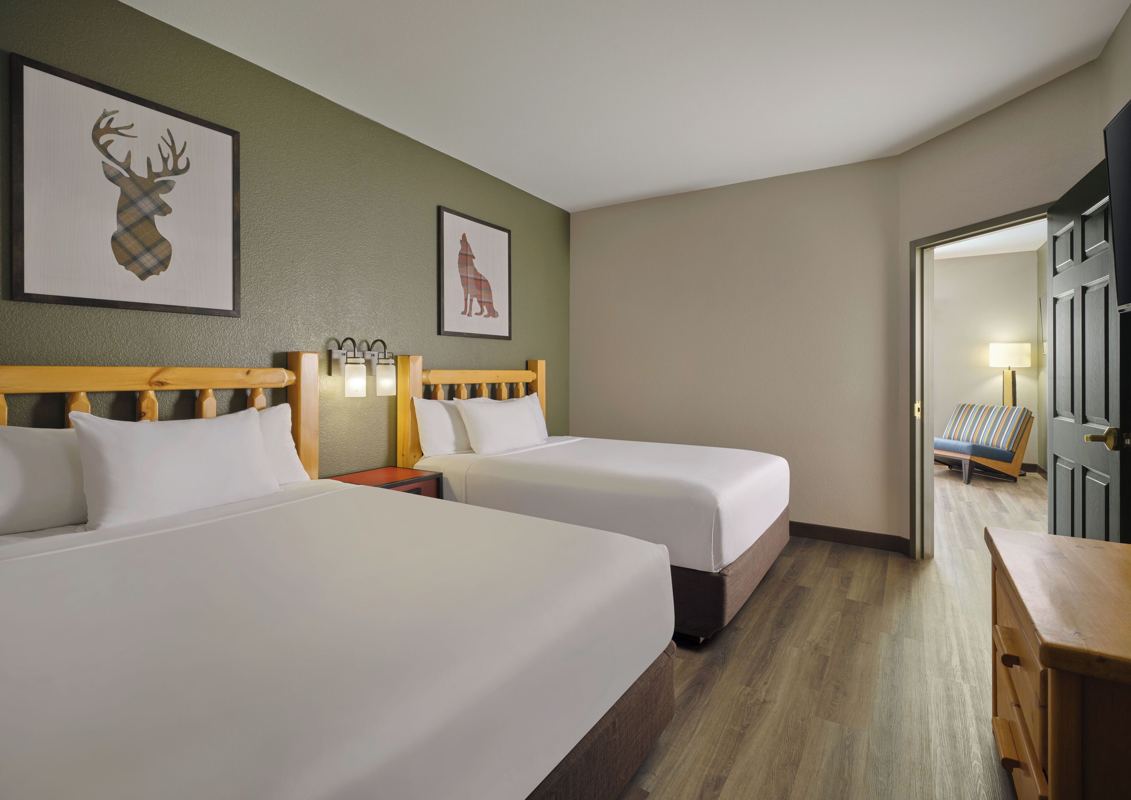 A hotel room with two beds, a wooden headboard, a nightstand with a lamp, and framed artwork on the wall.