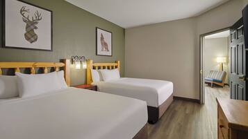 A hotel room with two beds, a wooden headboard, a nightstand with a lamp, and framed artwork on the wall.