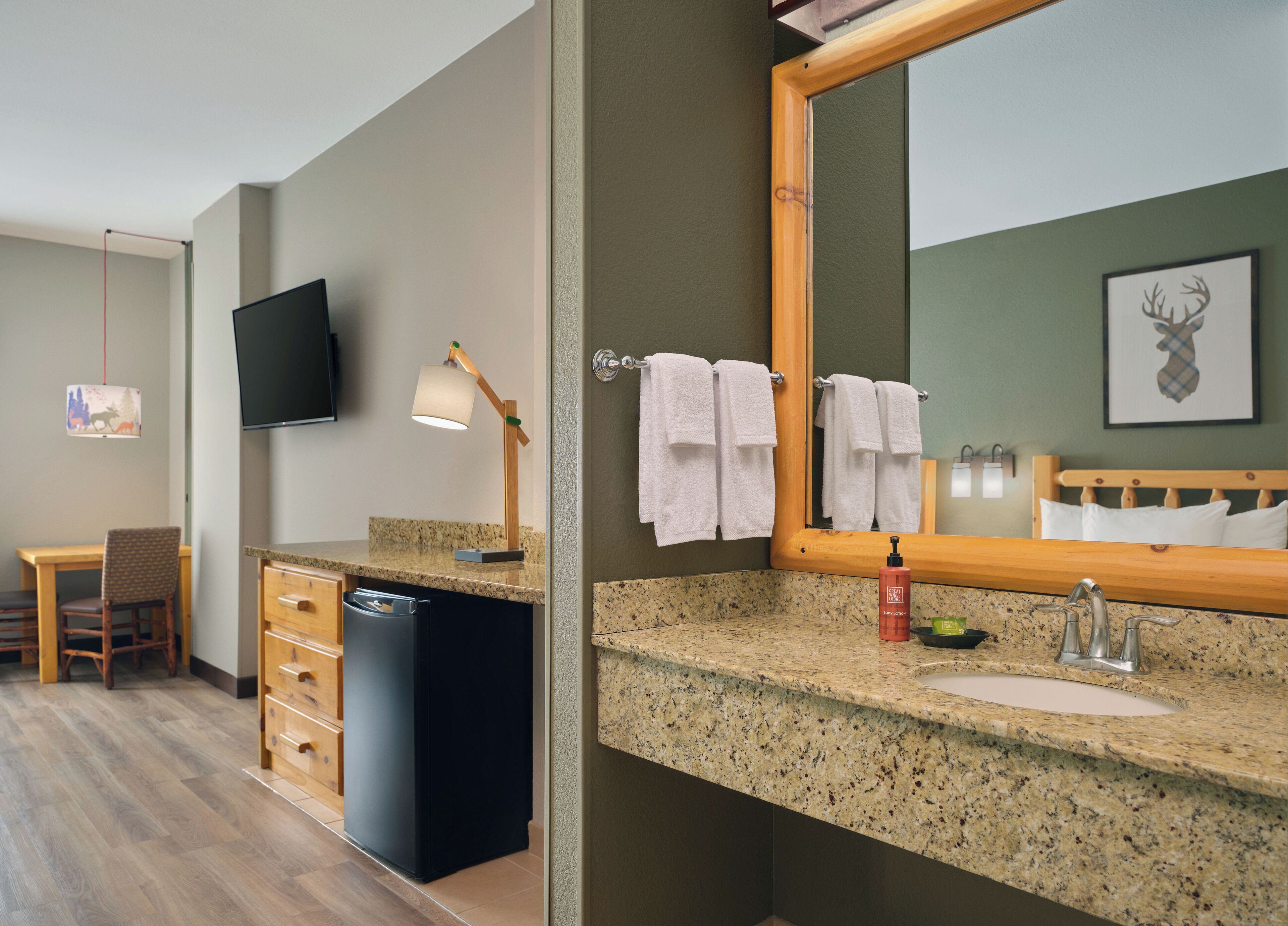 A hotel bathroom with a granite countertop, a sink, a mirror, and a television mounted on the wall.