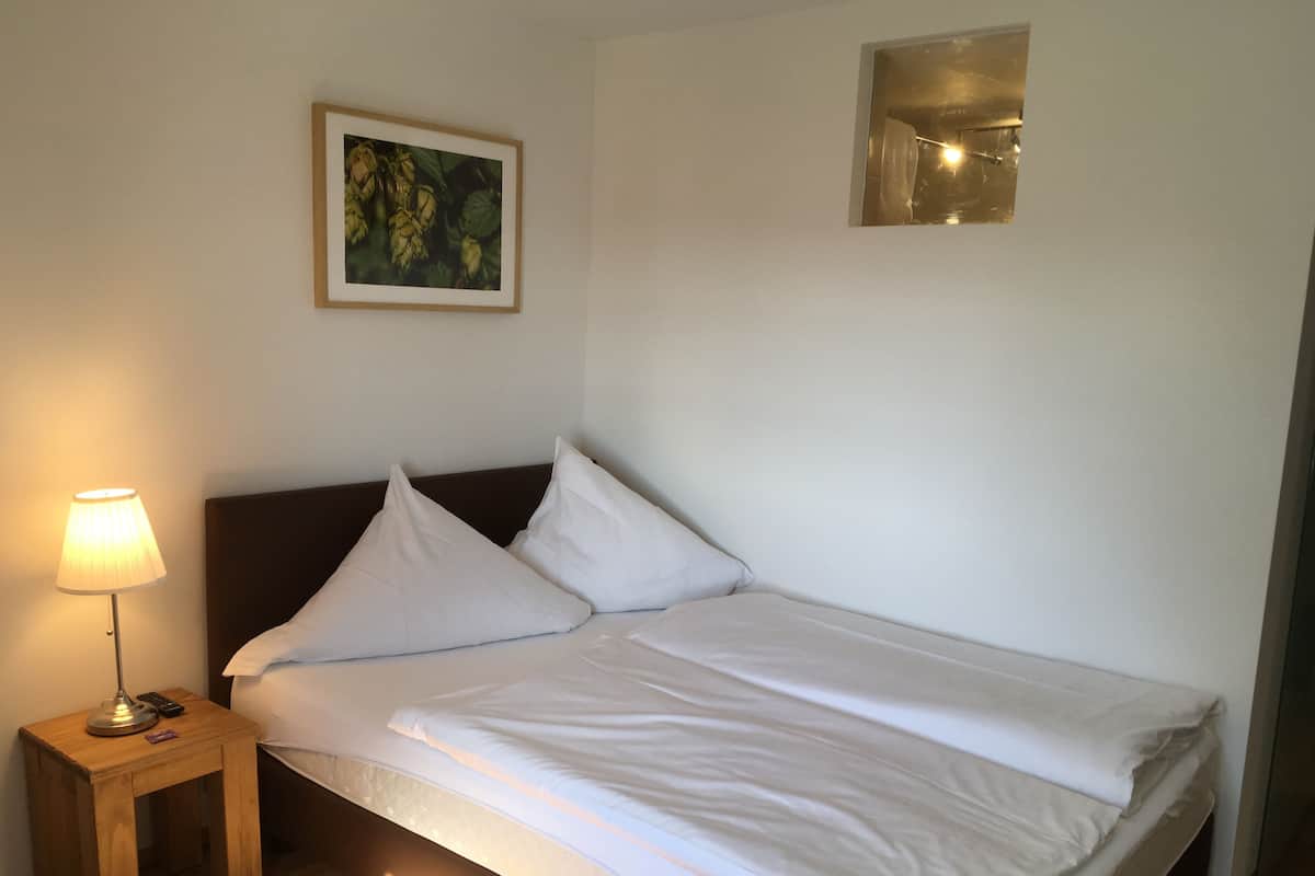A neatly made bed with white linens, a small bedside table with a lamp, and a framed picture on the wall.