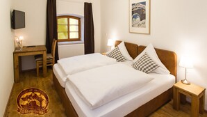 A hotel room with a double bed, a desk, a chair, a window with curtains, a wall-mounted TV, and a framed picture. - Brauereigasthof Stanglbräu (Hausen)