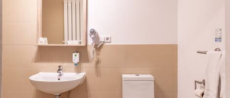 Un baño con lavamanos blanco, un espejo, inodoro y un perchero para toallas.