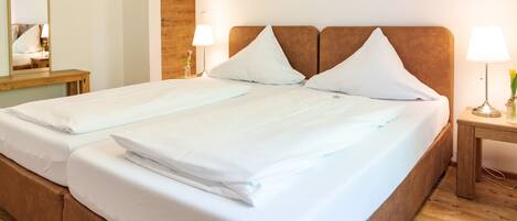 Cama doble con sábanas blancas y cabecera de madera en una habitación de hotel.