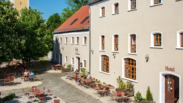 A hotel with a red-tiled roof, a church with a spire, and outdoor seating with tables and chairs. - Brauereigasthof Stanglbräu (Hausen)