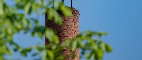 A bird nest on a brick tower with two birds, one standing and one flying.
