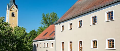 A hotel courtyard with outdoor seating, a church tower, and a cobblestone path.
