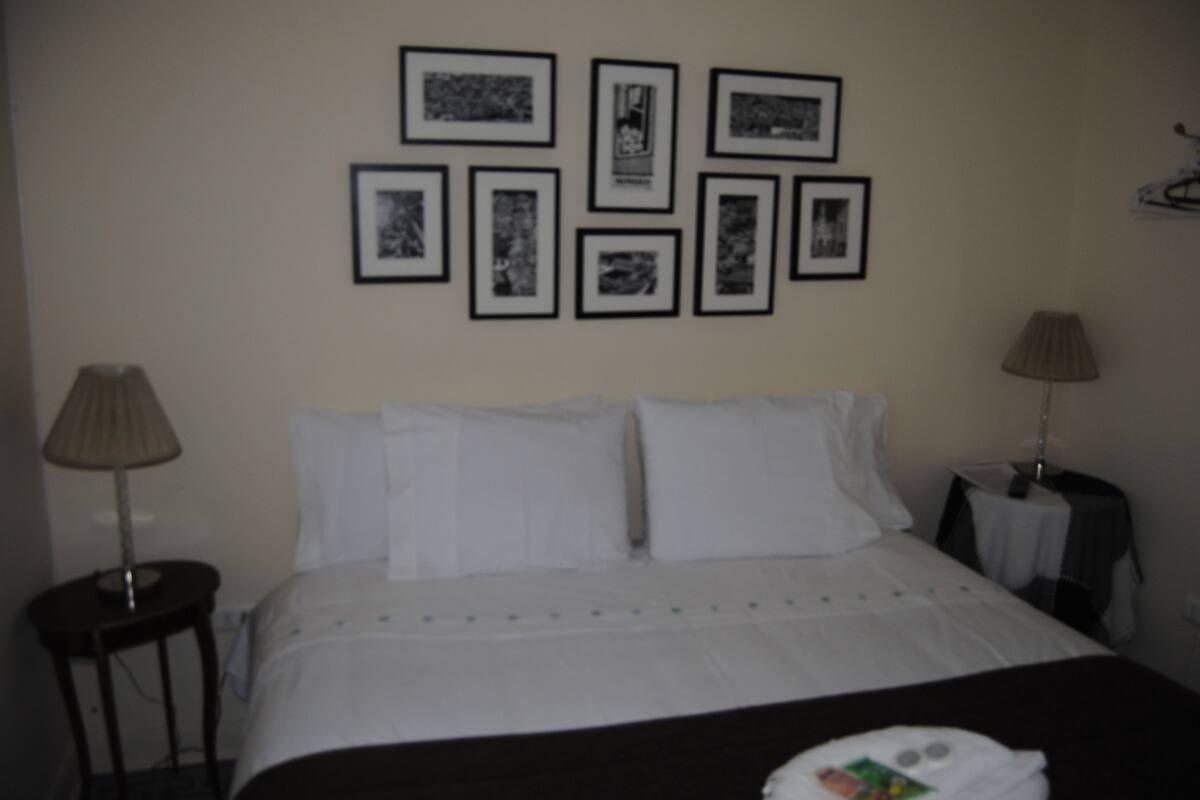 Quarto de hotel com uma cama, duas luminárias de cabeceira e uma parede com quadros.