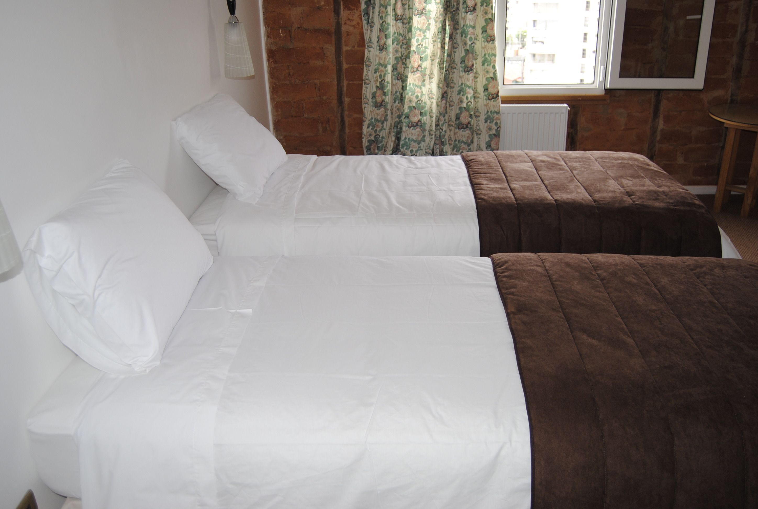 A room with two beds, one with white bedding and the other with brown bedding.