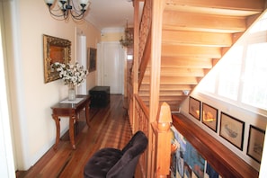 A hallway with wooden flooring, a staircase, a mirror, and framed pictures on the wall.
