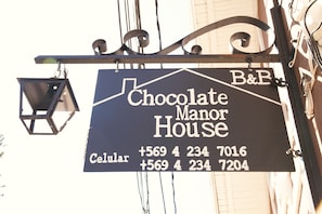 A sign for Chocolate Manor House with two phone numbers.