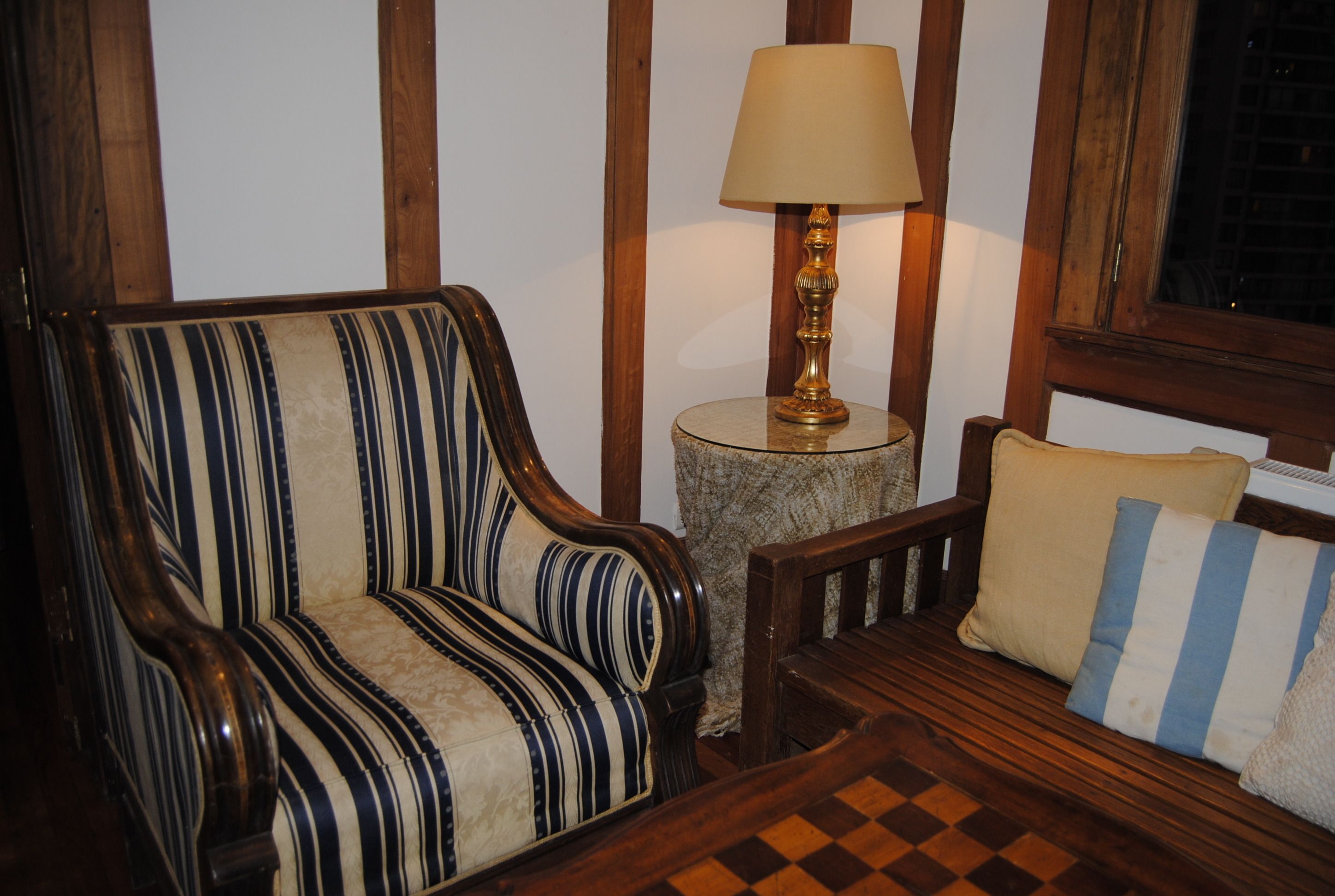 Un sillón a rayas, una mesita de madera con una lámpara y un pouf de cuadros.