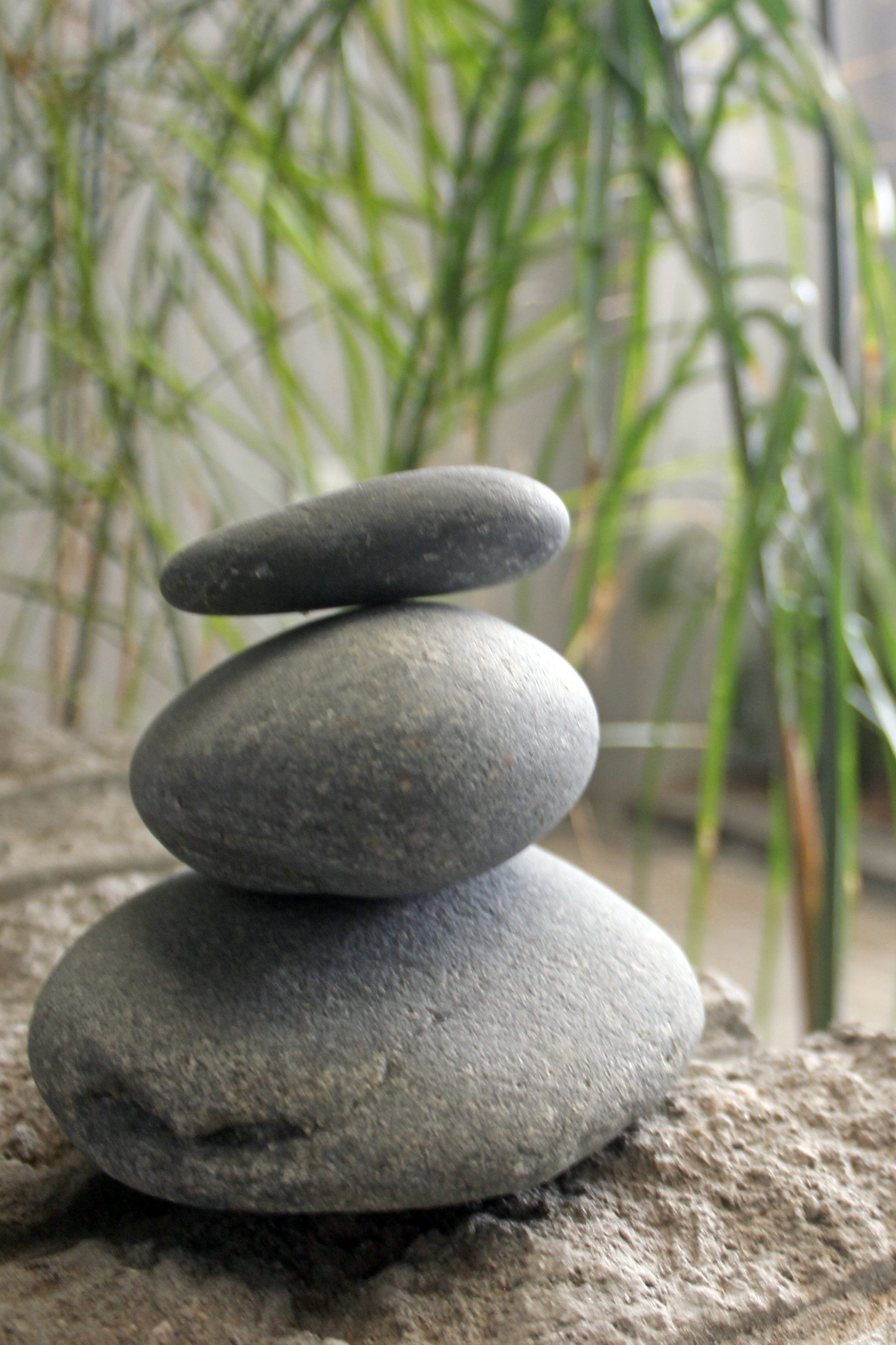 A stack of smooth, flat stones on a textured surface, with green plants in the background.