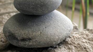 A stack of smooth, flat stones on a textured surface, with green plants in the background.